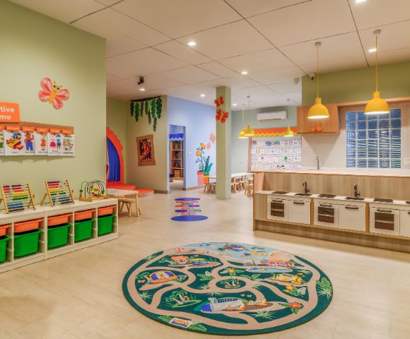 A bright, colorful preschool classroom with a playful, welcoming atmosphere. Features include educational materials, toy kitchen, vibrant decor, and creative-themed displays.