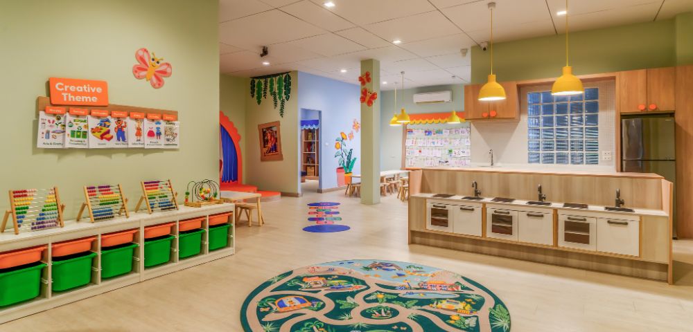 A bright, colorful preschool classroom with a playful, welcoming atmosphere. Features include educational materials, toy kitchen, vibrant decor, and creative-themed displays.