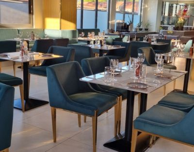 Modern restaurant interior with teal velvet chairs and marble tables set with glassware and cutlery. Soft, warm lighting creates a cozy atmosphere.
