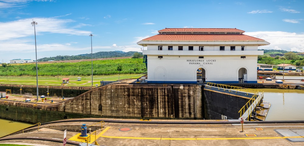 Panama Canal's Miraflores Locks on a sunny day, featuring the control building with a red-tiled roof, surrounded by greenery and blue skies.