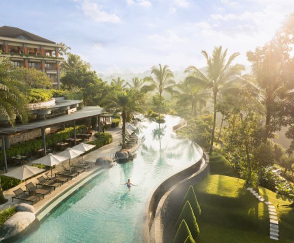 A serene infinity pool at a tropical resort, surrounded by palm trees and sun loungers, with a person swimming. Soft sunlight creates a tranquil ambiance.