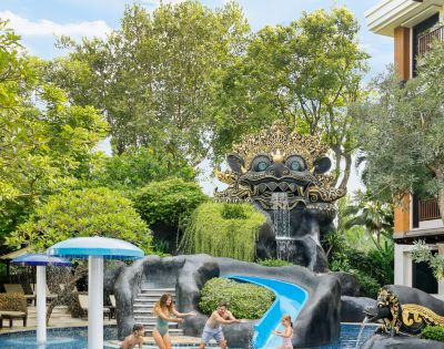 Ornate sculpture with a playful face over a waterfall and water slide in a lush, green garden. Vibrant, whimsical, and inviting atmosphere.