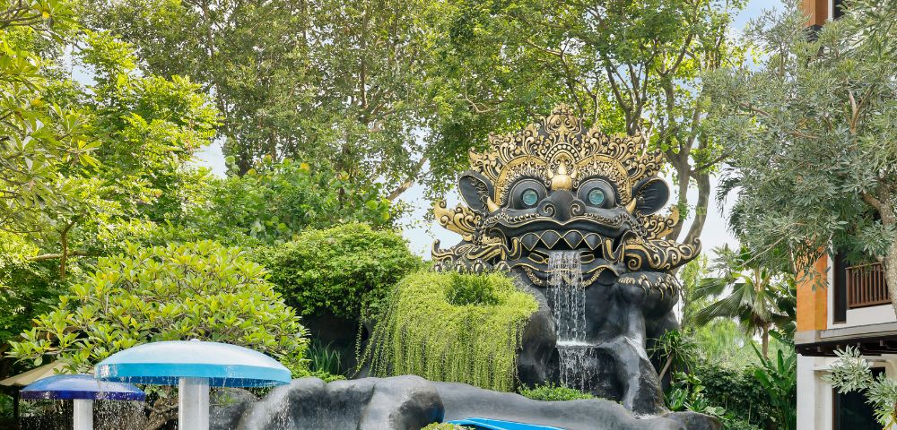 Ornate sculpture with a playful face over a waterfall and water slide in a lush, green garden. Vibrant, whimsical, and inviting atmosphere.
