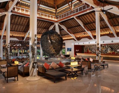 Spacious, elegant hotel lobby with high wooden ceilings, large circular sculpture, and comfortable seating. Warm lighting creates a welcoming atmosphere.