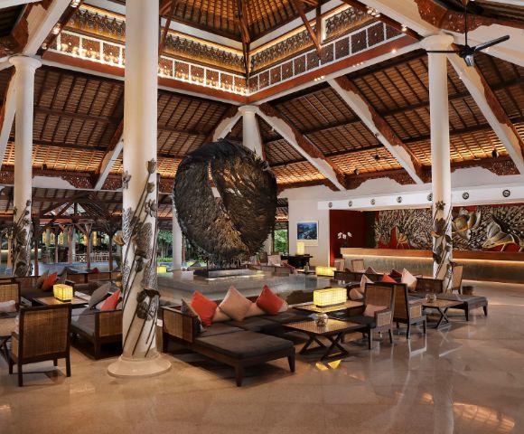 Spacious, elegant hotel lobby with high wooden ceilings, large circular sculpture, and comfortable seating. Warm lighting creates a welcoming atmosphere.