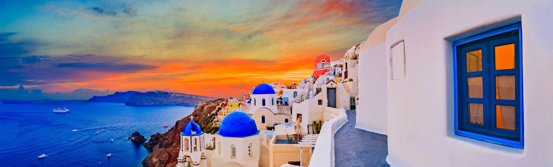Sunset view of Santorini, Greece, with white buildings and blue domes. The vibrant sky reflects on the sea, evoking a serene, picturesque ambiance.