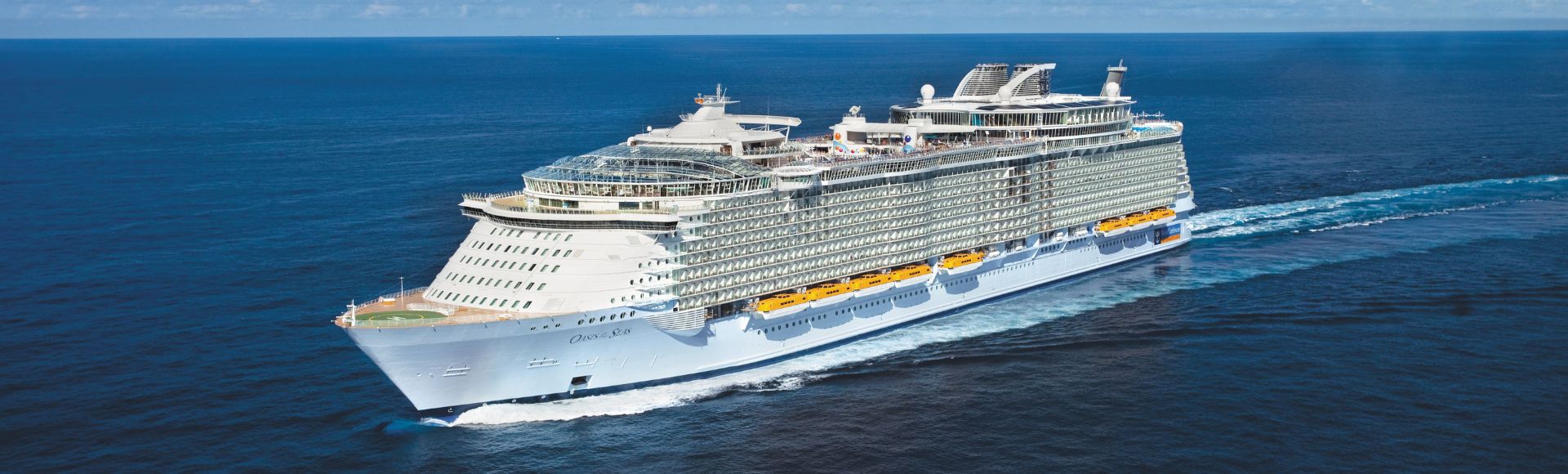 A large white cruise ship sails through a vast, calm ocean under a clear blue sky. The ship features multiple decks and geometric structures.