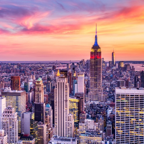 A vibrant New York City skyline at sunset, featuring the Empire State Building and colorful sky with pink, orange, and purple hues, conveying a lively urban atmosphere.