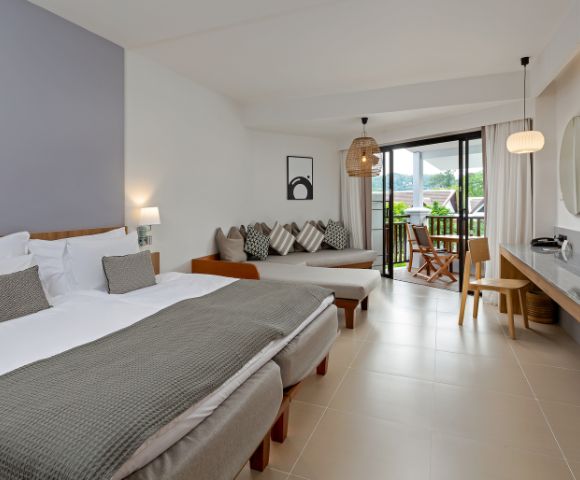 A modern hotel room features two beds with gray blankets, a cozy seating area, and a balcony view. The tone is serene and inviting, with soft lighting.