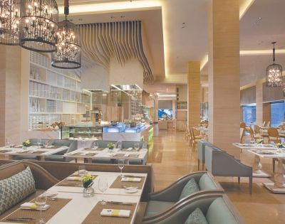 Elegant restaurant interior with modern decor, ambient lighting, and cushioned seating. Tables are set with white dishes and green accents, creating a welcoming atmosphere.