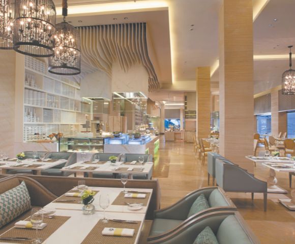 Elegant restaurant interior with modern decor, ambient lighting, and cushioned seating. Tables are set with white dishes and green accents, creating a welcoming atmosphere.