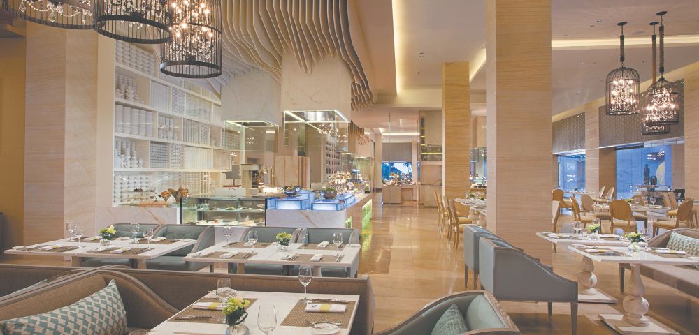 Elegant restaurant interior with modern decor, ambient lighting, and cushioned seating. Tables are set with white dishes and green accents, creating a welcoming atmosphere.