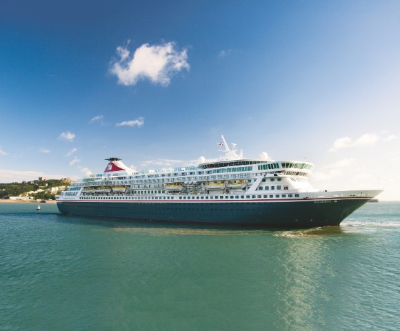 A large cruise ship sails in a calm, blue sea under a clear sky with a few clouds. The ship is white with a red funnel, conveying a sense of tranquility.