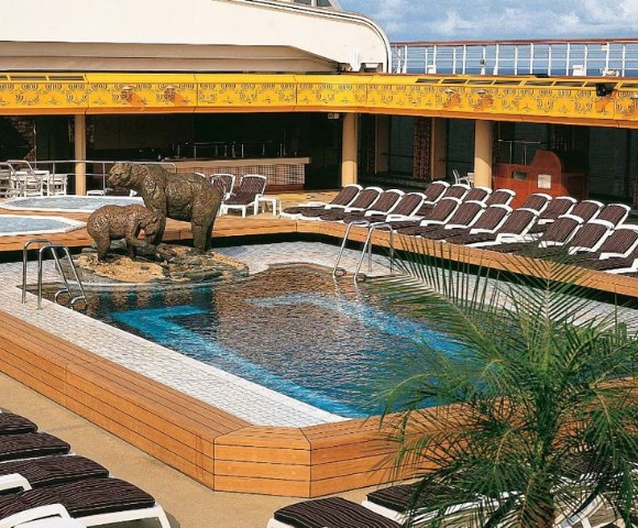 Rooftop pool area on a cruise ship features two jacuzzis, bear sculptures in the center, surrounded by lounge chairs. Sunny and inviting atmosphere.