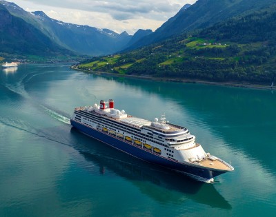 A large cruise ship sails through a calm fjord, surrounded by lush green hills and distant snow-capped mountains under a bright sky. Tranquil and majestic.