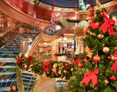 Festive interior with a decorated Christmas tree adorned with red bows and ornaments. Blue-carpeted staircase adds elegance to the warm, inviting scene.