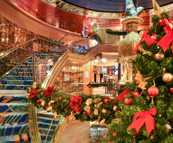 Festive interior with a decorated Christmas tree adorned with red bows and ornaments. Blue-carpeted staircase adds elegance to the warm, inviting scene.