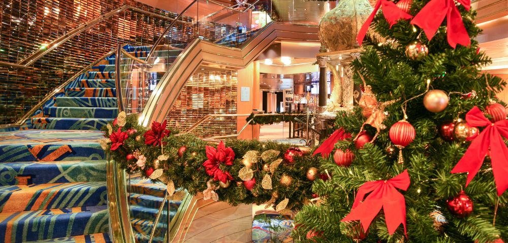 Festive interior with a decorated Christmas tree adorned with red bows and ornaments. Blue-carpeted staircase adds elegance to the warm, inviting scene.