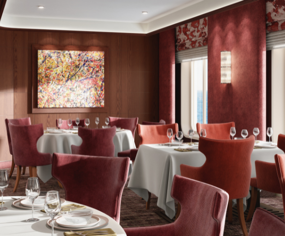 Elegant dining room with red chairs and white tablecloths, featuring a colorful abstract painting on a wooden wall. Large windows reveal an ocean view, creating a serene and sophisticated atmosphere.