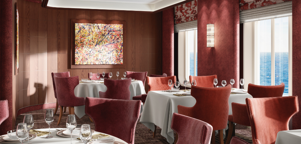 Elegant dining room with red chairs and white tablecloths, featuring a colorful abstract painting on a wooden wall. Large windows reveal an ocean view, creating a serene and sophisticated atmosphere.