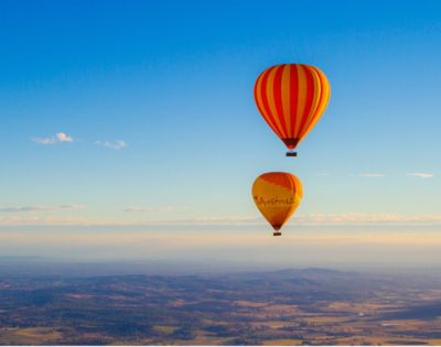 Two colorful hot air balloons float in a clear blue sky above a vast landscape. The scene conveys a sense of adventure and tranquility.