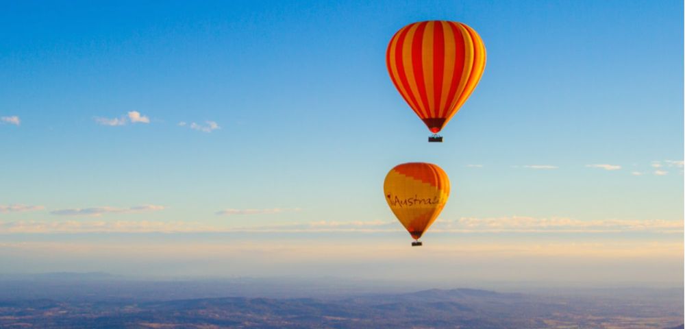 Two colorful hot air balloons float in a clear blue sky above a vast landscape. The scene conveys a sense of adventure and tranquility.