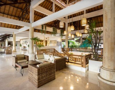 Spacious and airy hotel lobby with wicker furniture, hanging woven lamps, potted plants, and wooden beams, creating a warm and tropical ambiance.