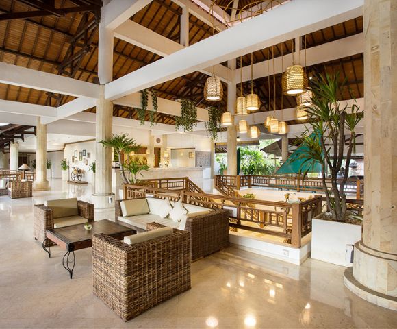 Spacious and airy hotel lobby with wicker furniture, hanging woven lamps, potted plants, and wooden beams, creating a warm and tropical ambiance.