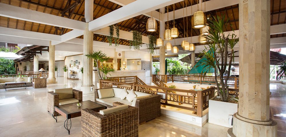Spacious and airy hotel lobby with wicker furniture, hanging woven lamps, potted plants, and wooden beams, creating a warm and tropical ambiance.