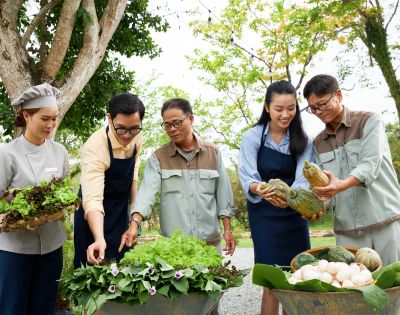 A diverse group of five people stands together outdoors, smiling and examining fresh vegetables and greens in baskets, conveying a sense of community and harvest.