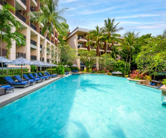 A serene hotel pool scene featuring clear blue water, surrounded by lush greenery and palm trees. Blue lounge chairs and striped umbrellas line the poolside.