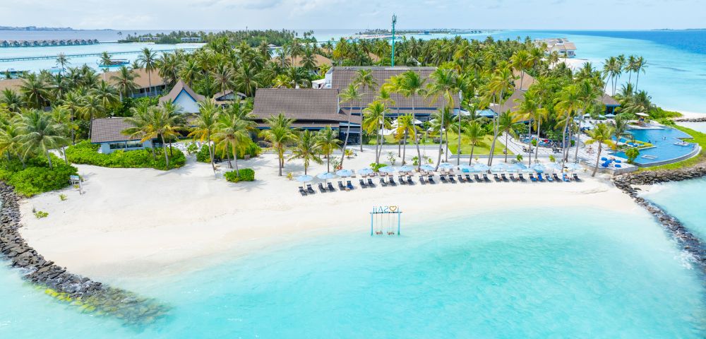 Tropical beach scene with turquoise water, white sand, and palm trees. Relaxed atmosphere with sun loungers facing the ocean under a blue sky.