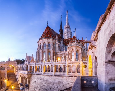Gothic-style Fisherman's Bastion in Budapest at twilight, featuring ornate arches, a colorful tiled roof, and illuminated arches, creating a serene atmosphere.
