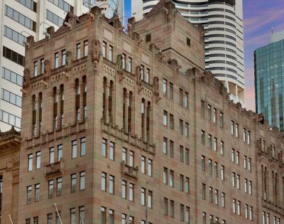 Historic brownstone building with ornate architectural details, set against a backdrop of modern skyscrapers under a pink and blue sky at dusk.