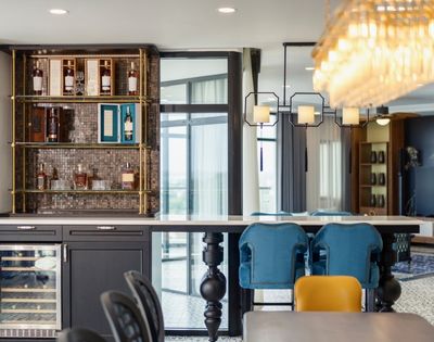 Modern kitchen with chic bar area, mosaic backsplash, and liquor shelves. Blue chairs at bar, elegant chandelier, creating a luxurious ambiance.