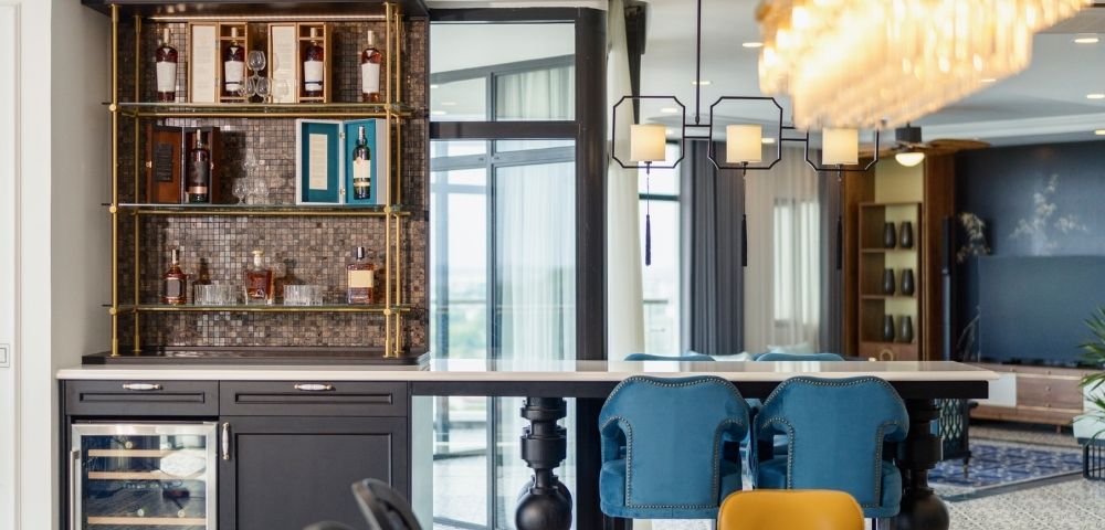 Modern kitchen with chic bar area, mosaic backsplash, and liquor shelves. Blue chairs at bar, elegant chandelier, creating a luxurious ambiance.