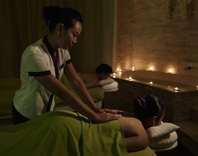 A massage therapist gives a back massage to a client in a dimly lit spa room. Candles softly illuminate the relaxing atmosphere.
