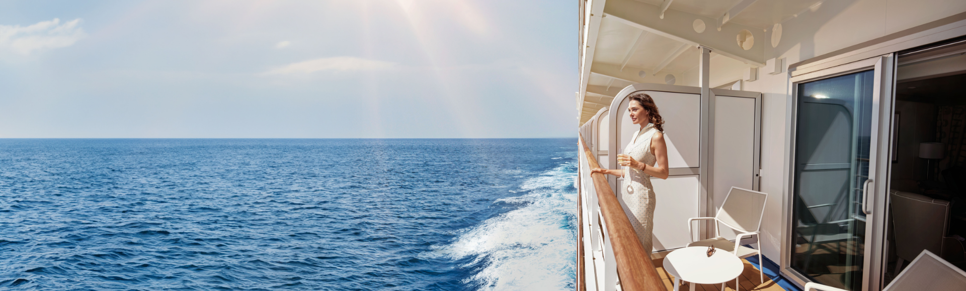 A woman stands on a cruise balcony, enjoying the serene ocean view under bright sunlight, with gentle waves in the distance.