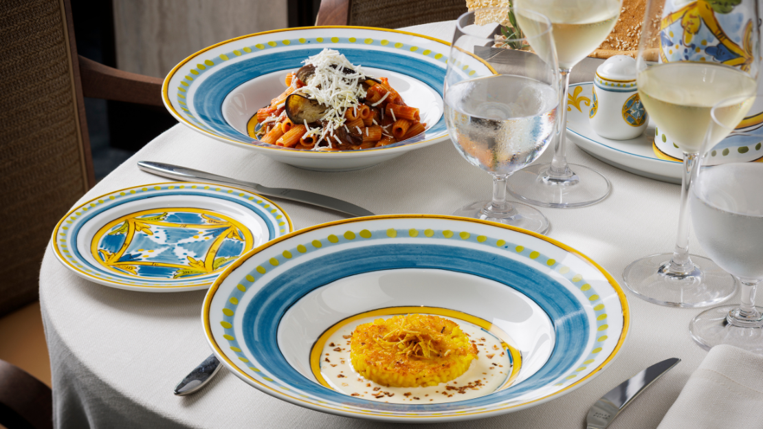 A beautifully arranged dining table featuring two artistic plates: one with creamy pasta and the other with a golden dessert.