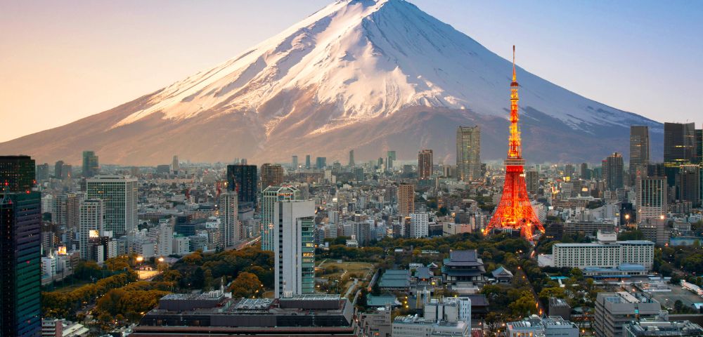 A stunning view of Tokyo skyline at sunset, featuring the illuminated Tokyo Tower in the foreground and majestic Mount Fuji in the background.