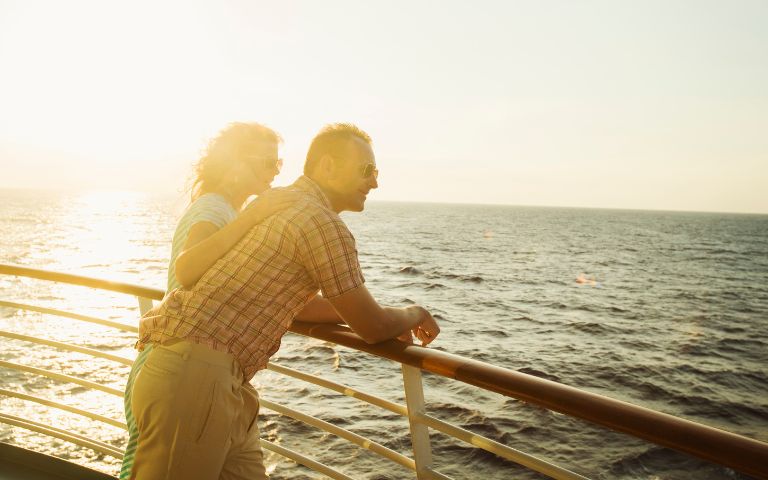 A couple enjoys a sunset together on a cruise ship, gazing at the ocean while leaning on the railing.