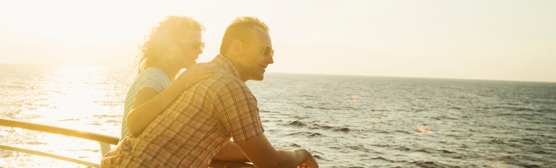 A couple enjoys a sunset together on a cruise ship, gazing at the ocean while leaning on the railing.