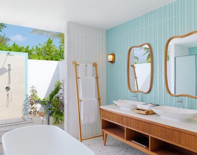 Modern outdoor bathroom with a tropical feel. Features twin wood-framed mirrors, double sinks, a freestanding tub, and an open-air shower. Bright and serene.