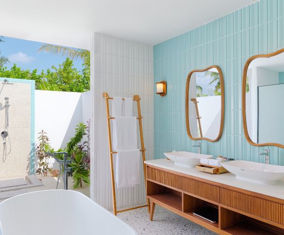 Modern outdoor bathroom with a tropical feel. Features twin wood-framed mirrors, double sinks, a freestanding tub, and an open-air shower. Bright and serene.