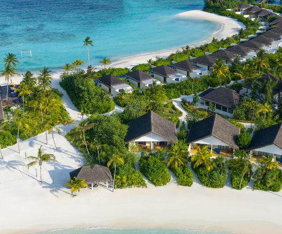 Aerial view of a tropical resort with white sandy beach in a crescent shape, turquoise water, and lush green palm trees, creating a serene and luxurious atmosphere.