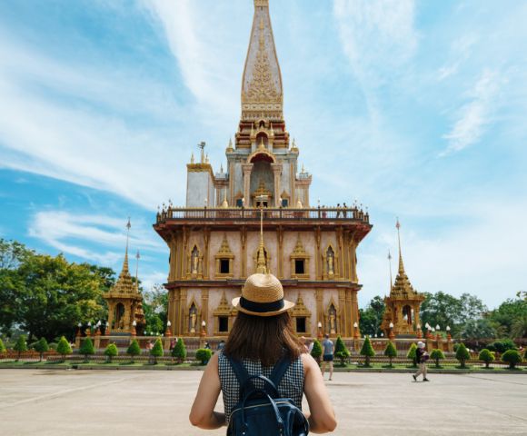 A person with a backpack stands before an ornate, golden temple against a bright blue sky, conveying a sense of awe and exploration.