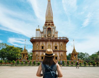 A person with a backpack stands before an ornate, golden temple against a bright blue sky, conveying a sense of awe and exploration.