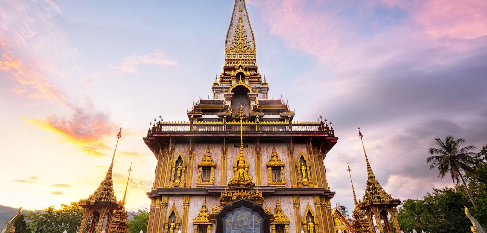 Ornate golden Thai temple with intricate carvings and peaked roof set against a colorful sunset sky, conveying serenity and grandeur.