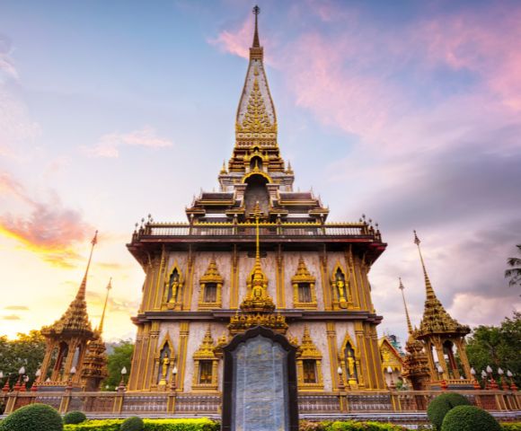 Ornate golden Thai temple with intricate carvings and peaked roof set against a colorful sunset sky, conveying serenity and grandeur.