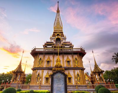 Ornate golden Thai temple with intricate carvings and peaked roof set against a colorful sunset sky, conveying serenity and grandeur.